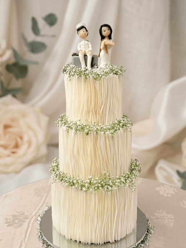 Three-tier white wedding cake with wafer-paper pleats, baby's breath garlands and a hand-modelled couple topper by Cake by O2, Colombo