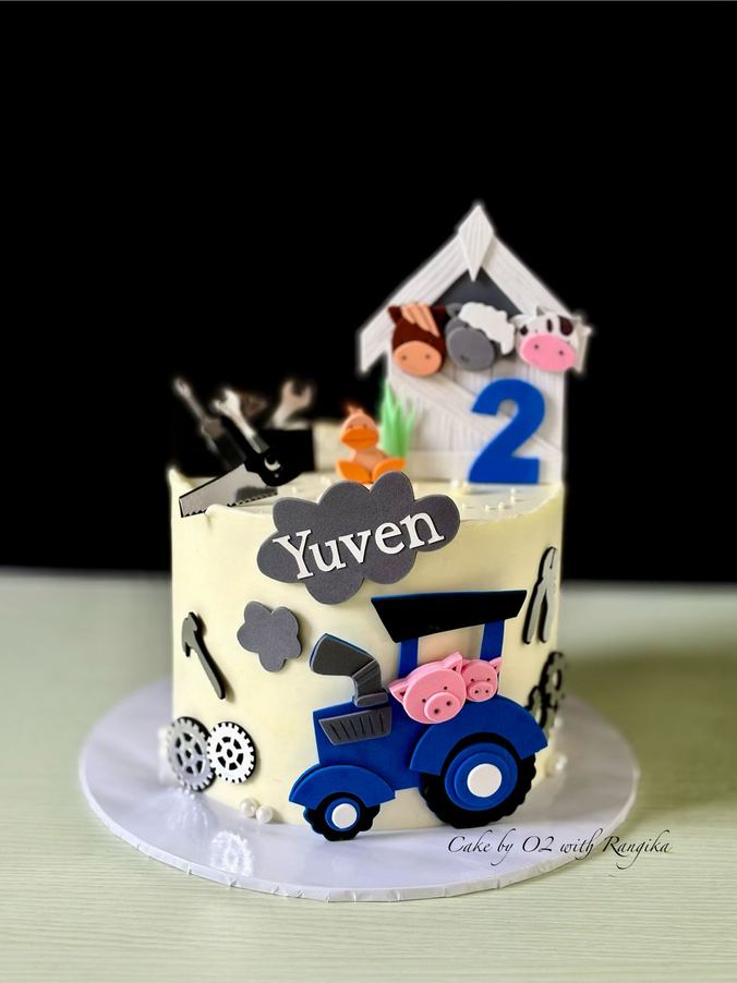 Farm-themed second birthday cake with a blue fondant tractor, pigs, barn animals, tools and the name Yuven, by Cake by O2